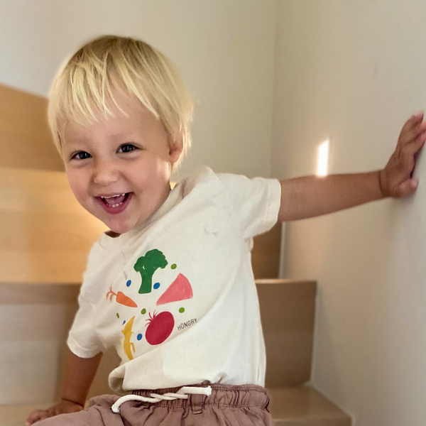 Kindje op trap met HONGRY kinder kledij T-shirt met patroon vele kleuren en vormen. 
